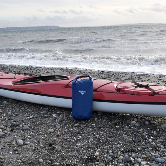 Red kayak on a pebbly beach with a blue bag attached, ocean waves in the background