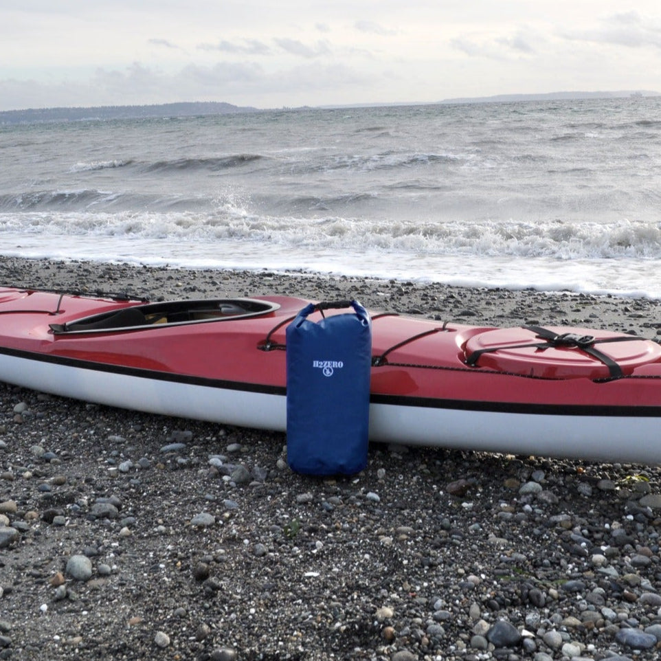 Red kayak on a pebbly beach with a blue bag attached, ocean waves in the background