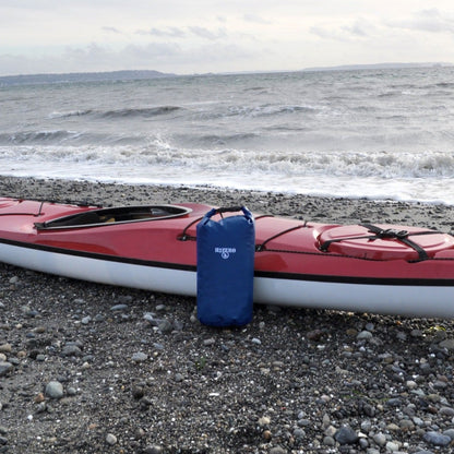 Red kayak on a pebbly beach with a blue bag attached, ocean waves in the background